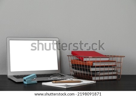 Metal holder with books, eyeglasses and laptop on table near grey wall
