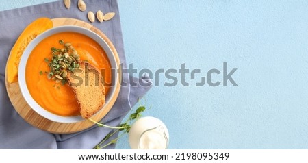Bowl of delicious pumpkin cream soup on light blue background with space for text