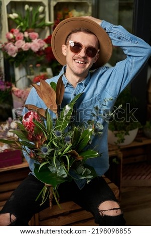 Mother's Day, Valentine's Day or International Women's Day concept. Hipster male person in sunglasses and hat with fresh spring flower bouquet in flower shop. High quality image