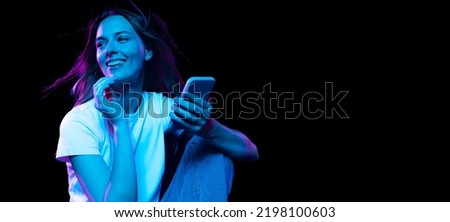 Online shopping. Happy young pretty girl with cellphone isolated on dark background in purple neon light. Concept of emotions, facial expression, youth, aspiration. Royalty-Free Stock Photo #2198100603