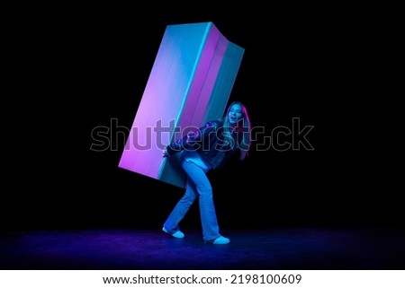 Last minute discounts. Young excited woman carries huge carton box isolated over dark background in neon light. Shopping, sales, ad, black friday, New Year and Christmas concept
