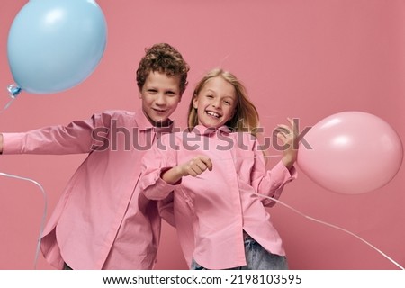 beautiful, happy children boy and girl stand on a pink background holding pink and blue balloons in their hands