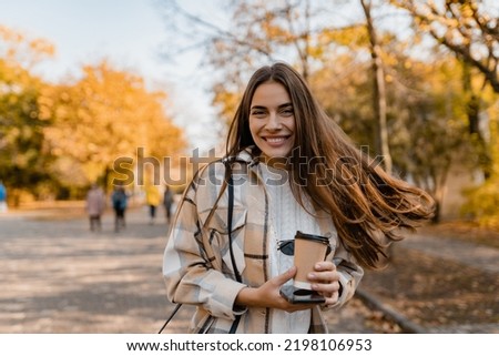 candid attractive young smiling woman walking in autumn park with coffee wearing checkered coat, happy mood, fashion style trend, long brown hair Royalty-Free Stock Photo #2198106953