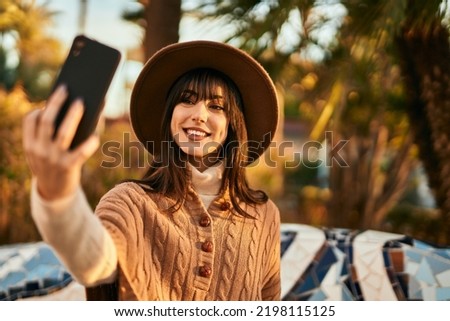 Brunette woman wearing winter hat taking a selfie picture with smartphone at the park