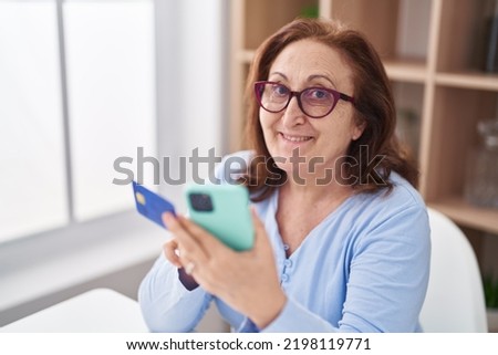 Senior woman using smartphone and credit card sitting on table at home