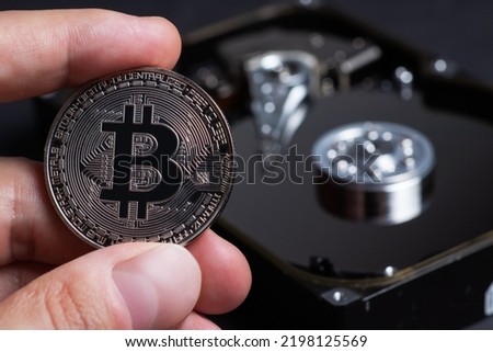 Silver Bitcoin coin in hand on background the opened HDD disk. Electronic money, cryptocurrency.