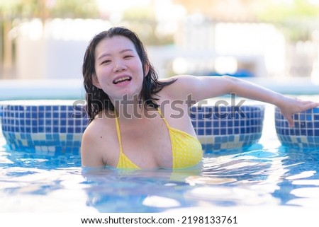 summer holidays natural portrait of young happy and attractive Asian Korean woman in yellow bikini enjoying swimming pool at hotel resort in tourism and travel concept