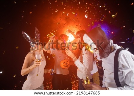 People dance at Halloween party with champagne glasses. Friends in the costumes in nightclub Royalty-Free Stock Photo #2198147685