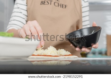 A woman in an apron prepares Margherita pizza in her kitchen.
