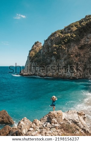 Beautiful girl sitting on a high rock and looking out to sea, panorama. Woman sits on the edge of cliff. The girl of the sea. Seascape. Woman at sunset. Sea tour. Copy space