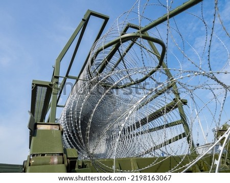 Process of installing barbed wire. Machine for laying barbed fence. Installation of barbed wire on state border. Installation of fence with spikes. Steel wire with spikes on background of sky