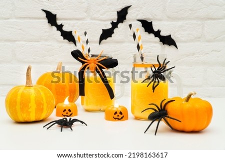 Pumpkin orange cocktails in glass jars, glasses decorated with scary spiders and a bat and eyes on a white table. happy halloween concept . Decorating a Halloween party with your own hands.