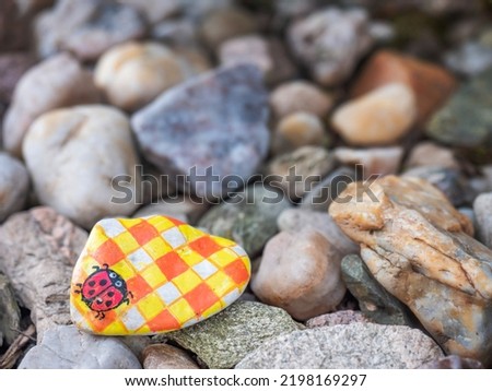 Ladybug painted on small pebble, children trail game. Hidden pebbles with painted pictures in vacation destination.