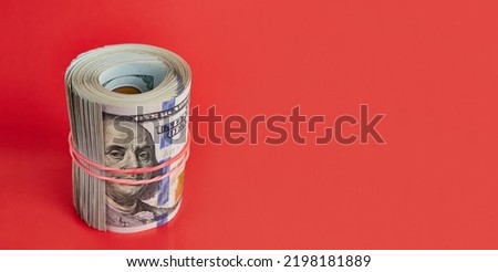 Many hundred dollar bills rolled up with a red rubber band on a red background.