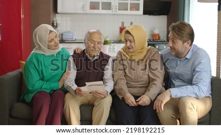 A Muslim Turkish family looking at old photos in their living room. The old father with his children and his hijab wife are happy looking at old photos.