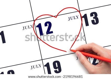 12th day ofJuly. A woman's hand drawing a red heart shape on the calendar date of 12 July. Heart as a symbol of love. Summer month. Day of the year concept