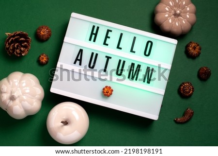 Autumn card with hello autumn text, pumpkins, pine cones and autumn decor on dark green background