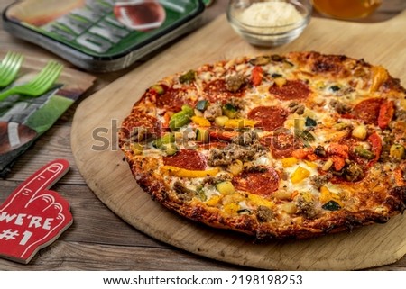Close up of cauliflower crust pizza with sausage, pepperoni, peppers, onions, zucchini, cheese and tomato sauce sitting on wooden pizza peel, surrounded by football themed party plates and napkins