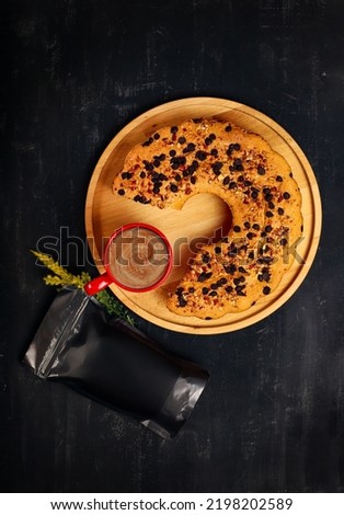 Round homemade cake on wooden tray on black background with filter coffee in red mug and black coffee packaging next to it. top view coffee package mockup. coffee bean package mockup Royalty-Free Stock Photo #2198202589