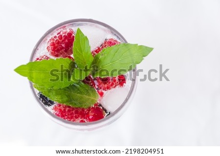 Carbonated drinks with fresh berries and ice. Fresh cold sparkling bubble water with mint, raspberry, black and red currant in transparent glass with ice, top view macro. Food and drink concept