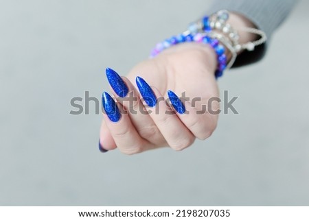 Woman's beautiful hand with long nails and bright blue manicure with bottles of nail polish