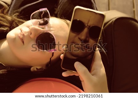 a girl in sunglasses lies on the knees of men. Reflection of a guy on a smartphone monitor. relaxing couple. chill out outdoor. 
