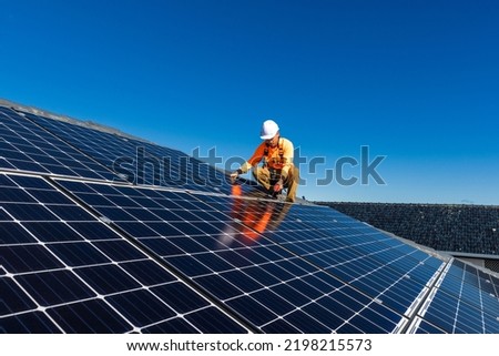 Solar panel technician with drill installing solar panels on house roof on a sunny day. Royalty-Free Stock Photo #2198215573