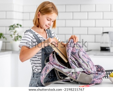Preteen girl preparing backpack for school class lessons at home and put notebook inside. Female pupil with schoolbag and college supplies Royalty-Free Stock Photo #2198215767