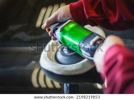 Car detailing - hands with an orbital polishing machine in an auto repair shop. Selective focus. A man polishes a car with a close-up grinder. 
