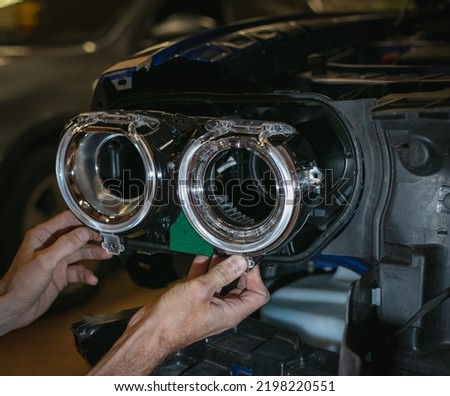Car headlight in repair close-up. The car mechanic installs the lens in the headlight housing. The concept of a car service.Installation of LED lenses in the headlight. LED lens.Restoration of optics. Royalty-Free Stock Photo #2198220551