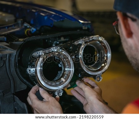 Car headlight in repair close-up. The car mechanic installs the lens in the headlight housing. The concept of a car service.Installation of LED lenses in the headlight. LED lens.Restoration of optics. Royalty-Free Stock Photo #2198220559
