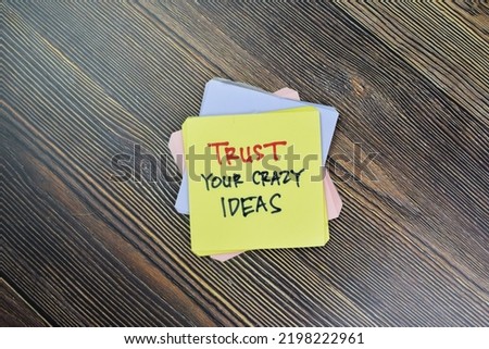 Concept of Trust Your Crazy Ideas write on sticky notes isolated on Wooden Table.