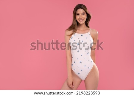 Happy young brunette woman smiling to the camera, posing on pastel pink studio background. A lot of copyspace. Female model with fit, slim body.

