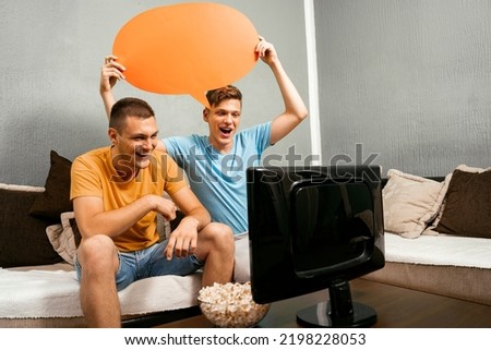 Two young adults looking basketball on tv one holding speech bubble over head , copy space 