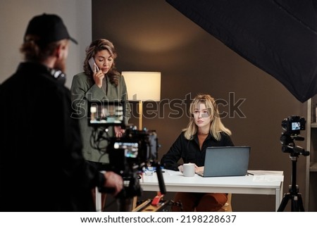 Two young intercultural female models using mobile gadgets during commercial being shot by videographer with steadicam Royalty-Free Stock Photo #2198228637