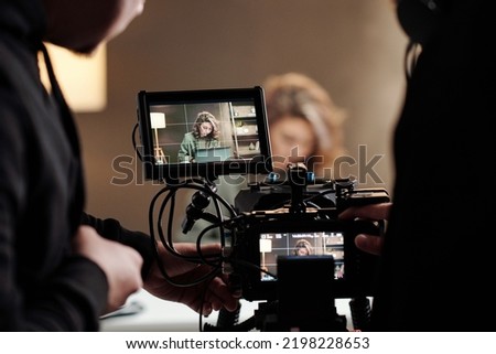 Close-up of steadicam screens with female model using laptop by table during commercial being shot by cameraman and his assistant Royalty-Free Stock Photo #2198228653
