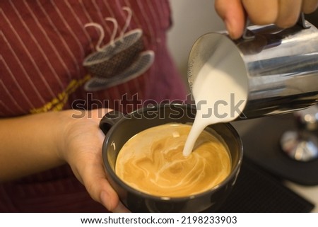 close up picture of barista pouring milk on coffee to make hot cup of latte