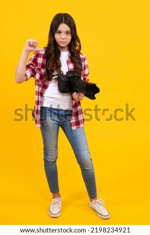 Full length of teenager girl with dslr professional photo camera with big photo lens. Child photographer isoalted on yellow background. Photo school. Shooting on professional camera.