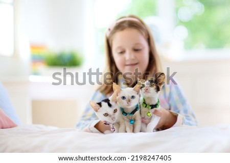Child playing with baby cat on bed in white bedroom. Kid holding white kitten. Little girl in pajamas with cute pet animal at home. Kids play with cats. Children and domestic animals pets.
