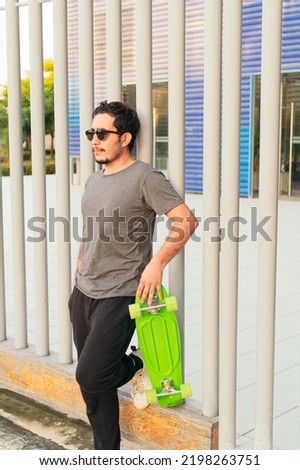 Hispanic man with sunglasses and skateboard in the park on a sunny day.