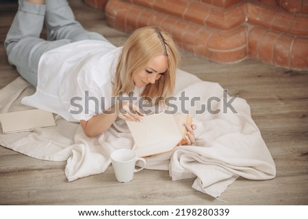 Young adult woman is reading a book on the floor in the interior.