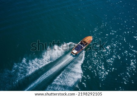 Classic wooden boat with motor moving on blue water aerial view. Italian wooden boat fast moving diagonal top view. An expensive wooden boat is an average movement on the water. Royalty-Free Stock Photo #2198292105
