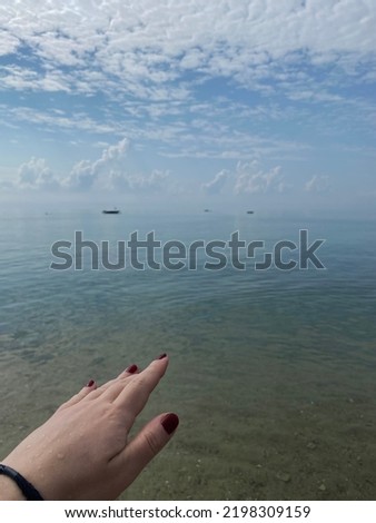 Magnificent photo of deep blue sky and Stratus clouds on a sunny day by the sea, calm sea and photo of female hand with burgundy nail polish reaching into the sea, natural nature shot