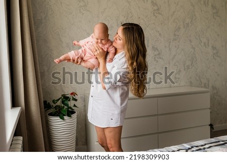 Mom with her baby newborn infant kid child at home take care in the bedroom put on clothes. Woman family women's health and maternity