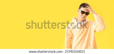 Teenage boy with headphones on yellow background with space for text