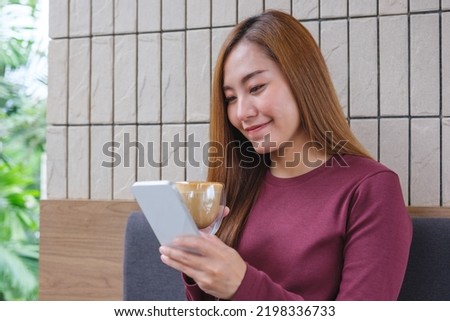 Portrait image of a young woman holding and using mobile phone while drinking coffee in cafe
