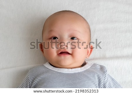 A baby in a striped shirt lies smiling on the white carpet.