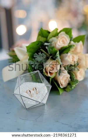 A pair of beautiful wedding rings in a modern glass stand and a delicate bridal bouquet of roses. Marriage, ceremony. Soft selective focus.