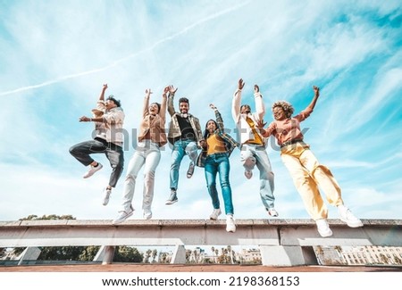 Group of young people enjoying freedom together - Happy multicultural friends jumping on city street - Happiness concept with guys and girls raising arms up to the sky Royalty-Free Stock Photo #2198368153