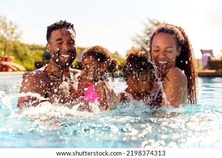 Family On Summer Holiday With Two Girls Being Held In Swimming Pool By Parents And Splashing Royalty-Free Stock Photo #2198374313